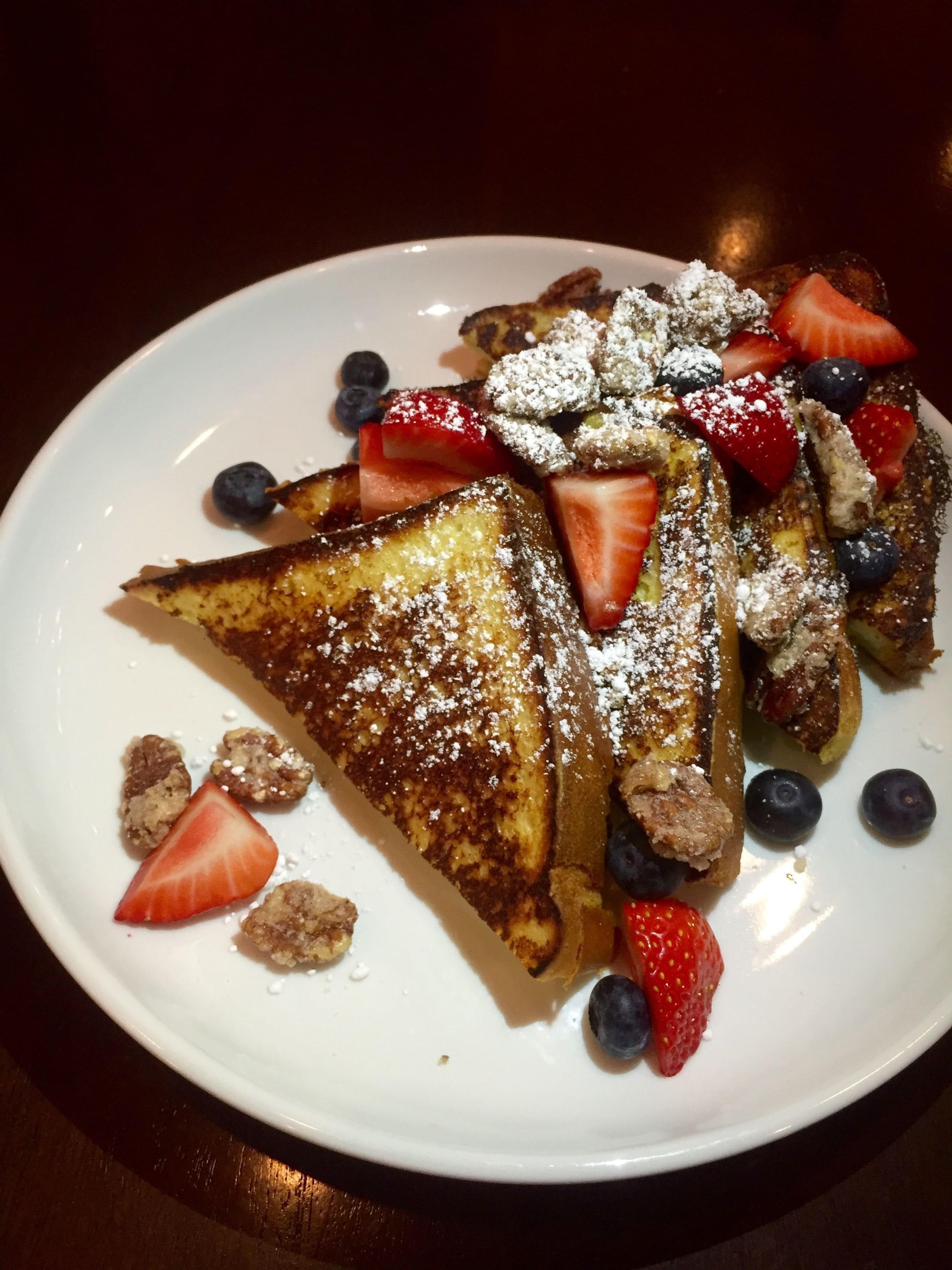 A plate of French toast with strawberries and blueberries, dusted with powdered sugar.