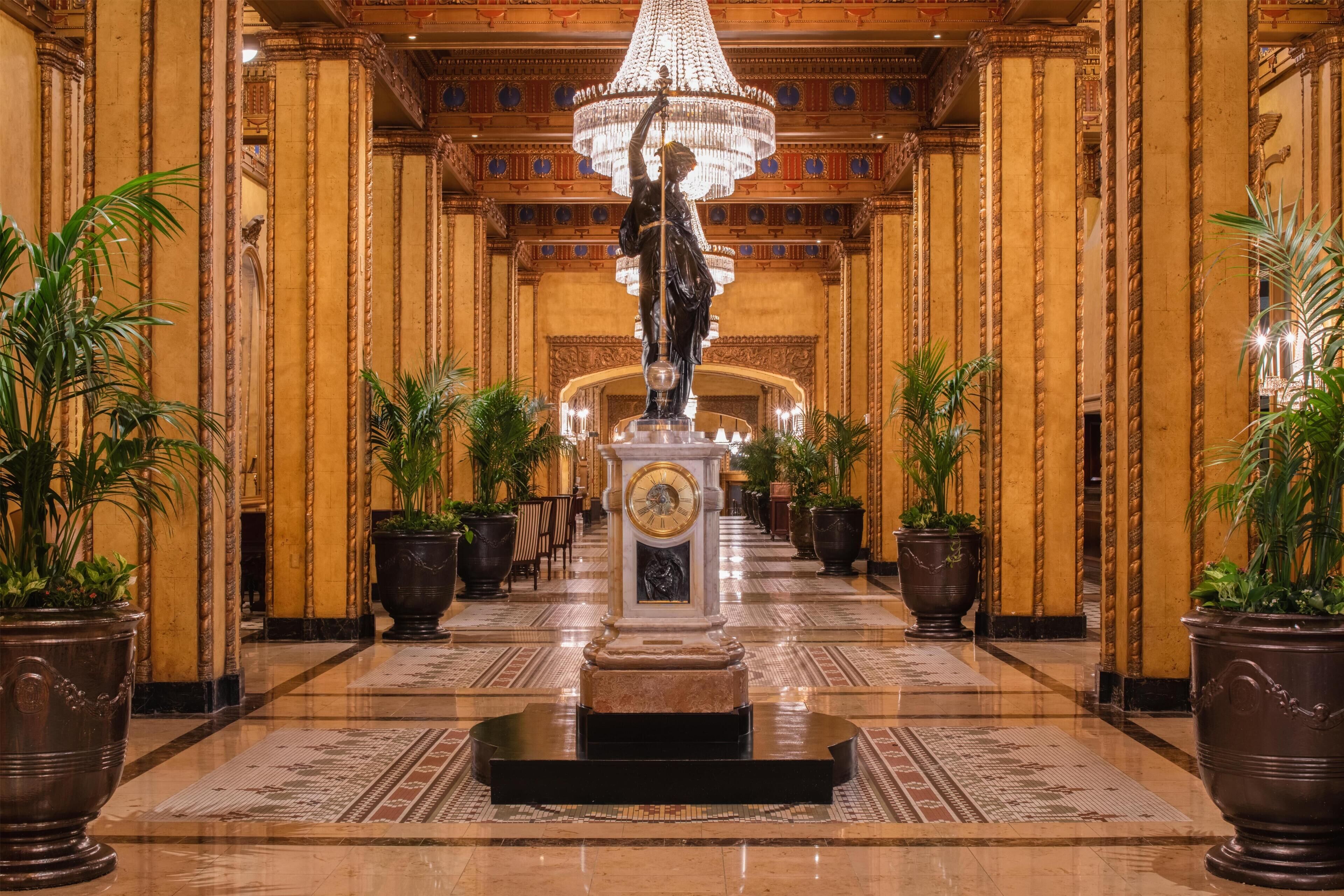 Un vaste hall d’entrée avec une statue centrale, des colonnes richement décorées et un lustre.