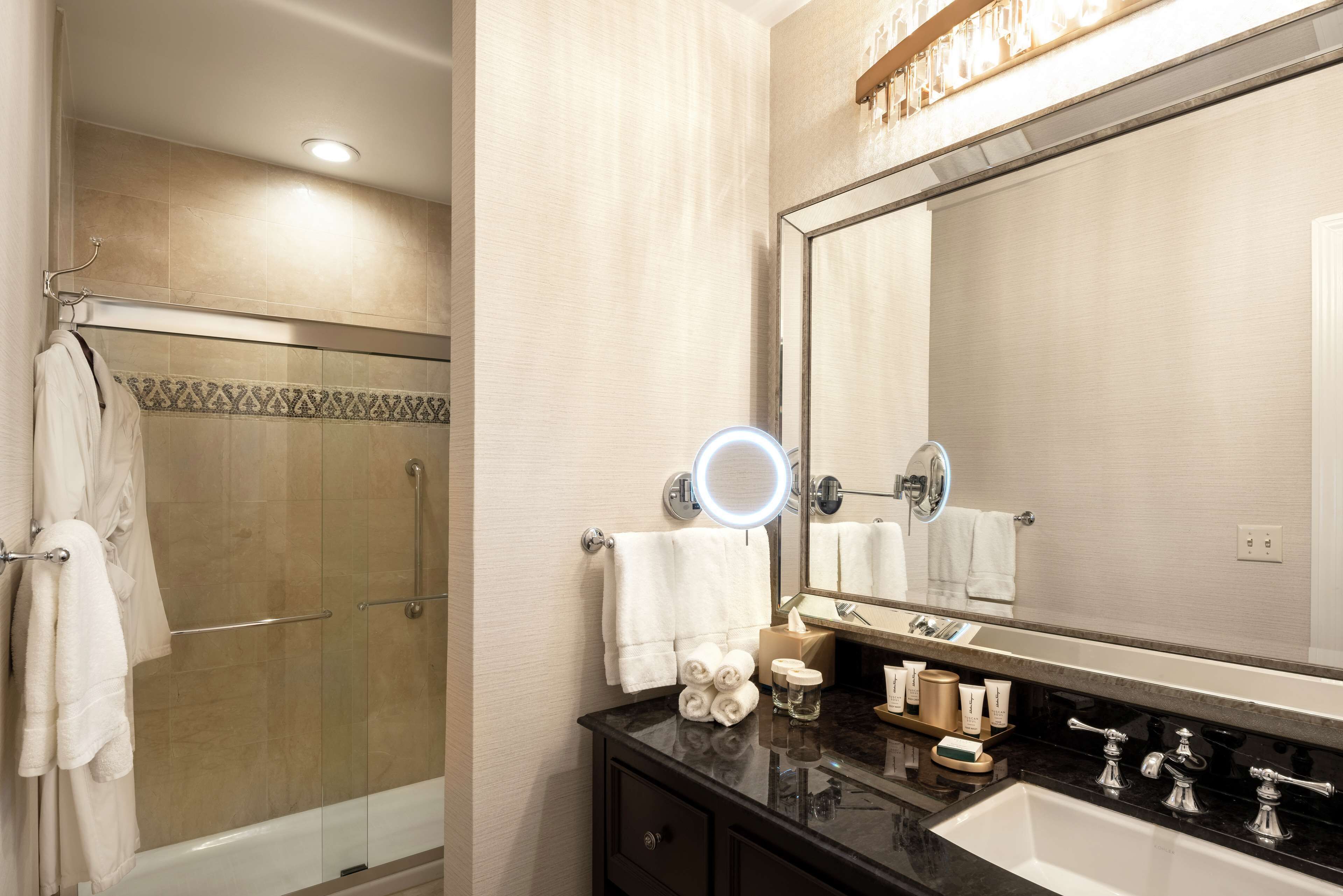 Une salle de bain dotée d’un grand miroir, d’un plan de toilette noir et d’une cabine de douche en verre.