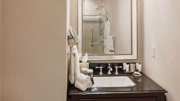 A bathroom with a white toilet, a dark brown vanity with a large mirror, a chandelier above the mirror, and a towel rack with folded towels.
