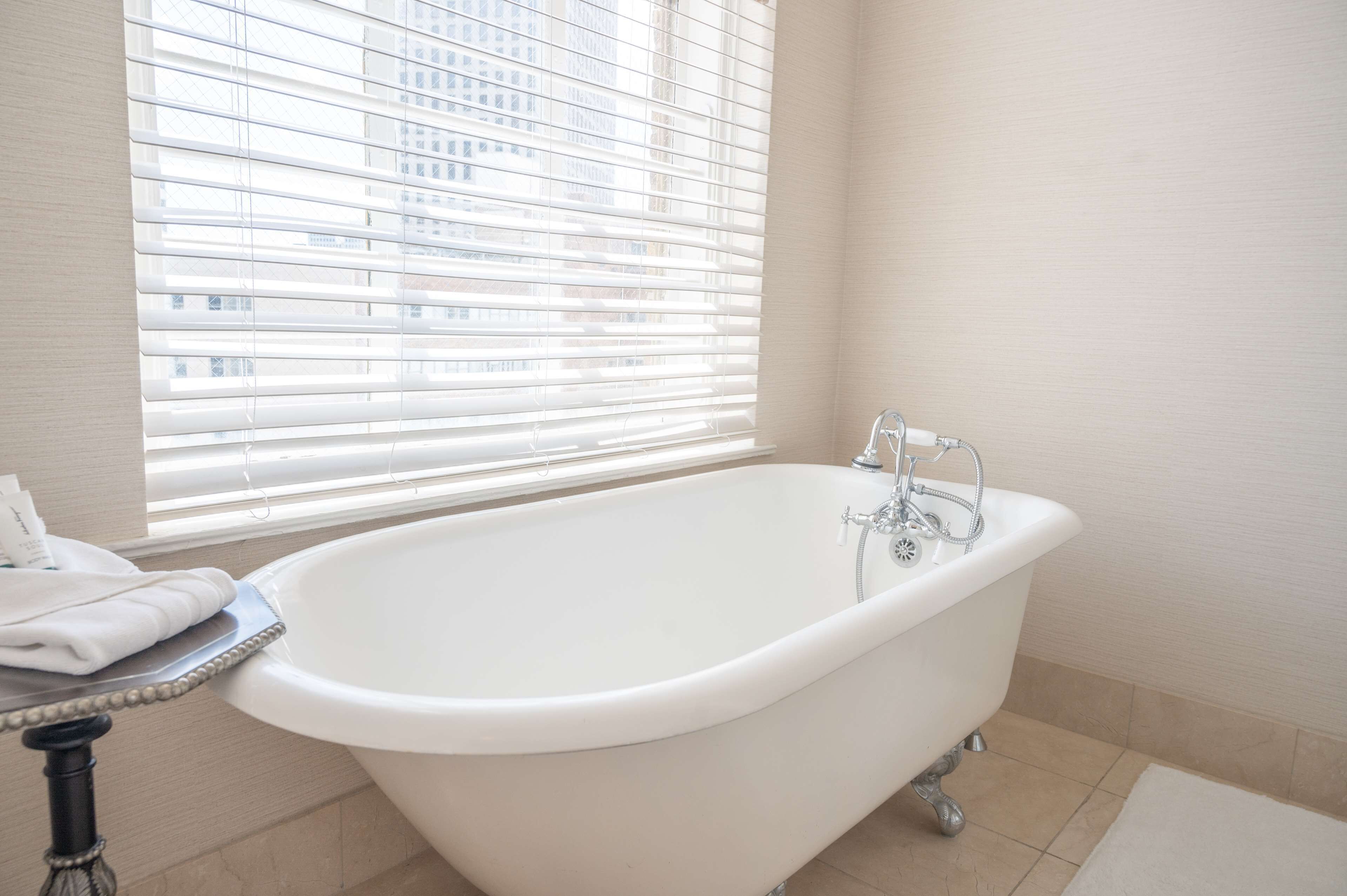 A modern bathroom with a freestanding bathtub, a window with blinds, and a towel rack.