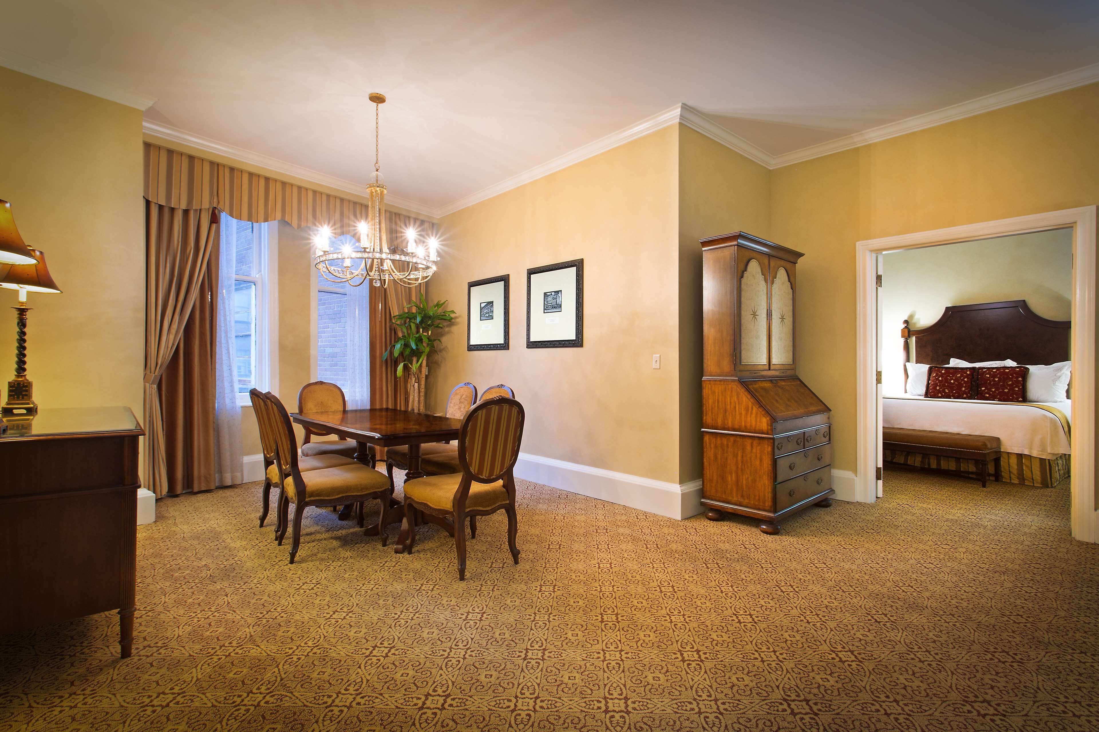 A hotel room with a dining area, a large wooden cabinet, and a bed with a headboard.
