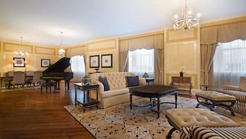Uma sala de estar ampla com um piano de cauda, um sofá, uma mesa de centro e poltronas listradas.