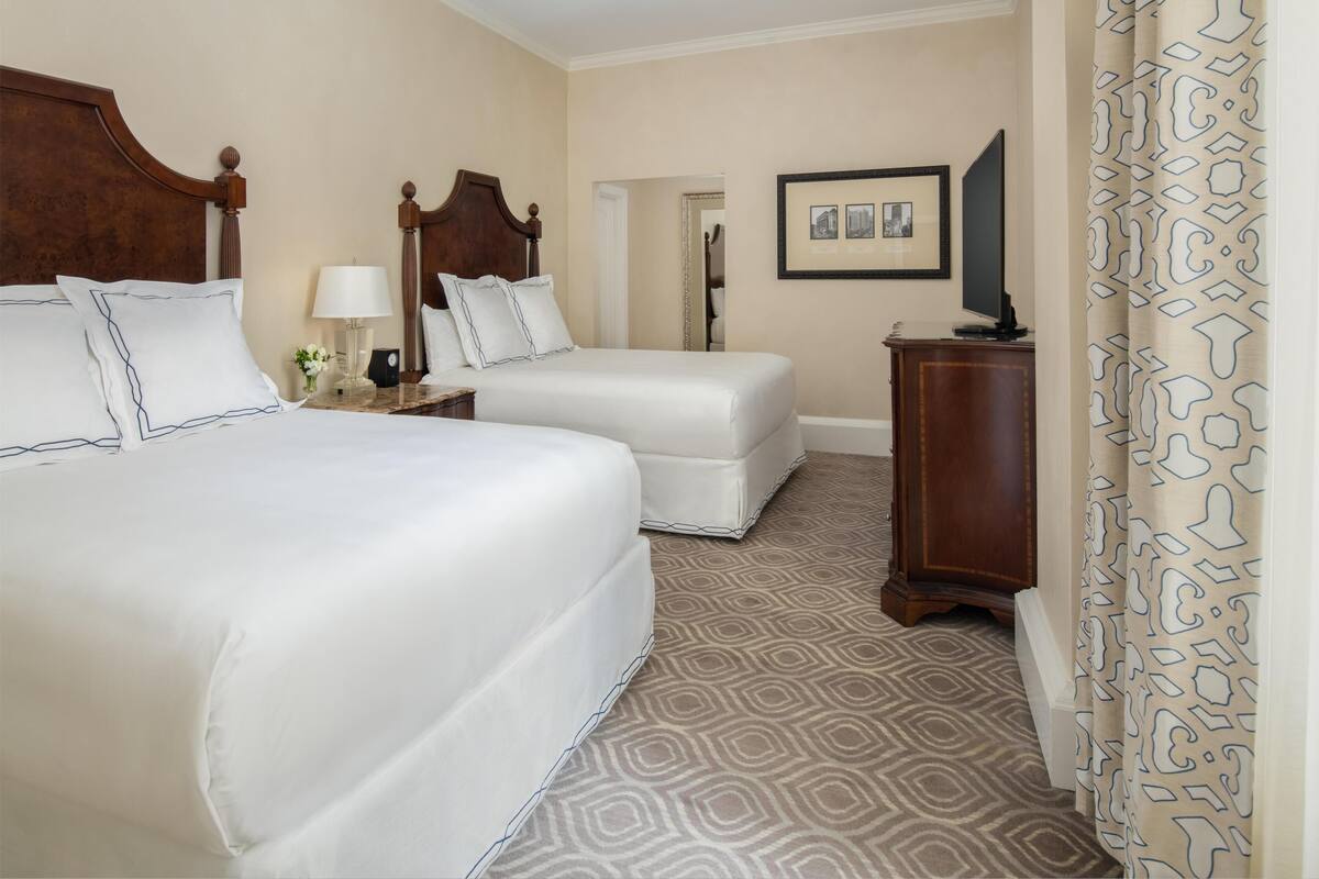 Een hotelkamer met twee bedden, een nachtkastje, een lamp, een televisie en een kamerbreed tapijt met een patroon.