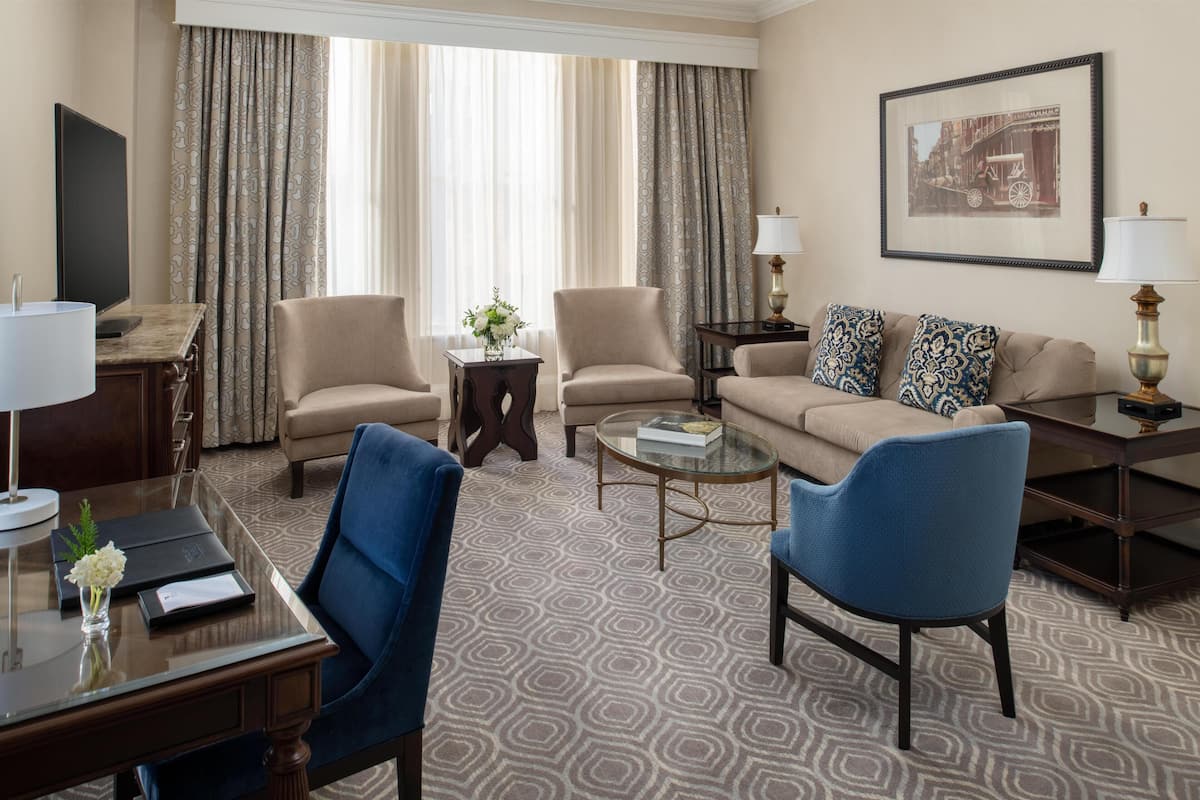 Hotelkamer met een bank, twee fauteuils, een salontafel, een bureau met lamp, een televisie en een lijst aan de muur.