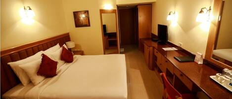 Una habitación de hotel con cama, escritorio, silla, televisor y espejo.