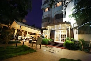 A hotel with a well-lit entrance, outdoor seating area, and a staircase leading to the main building.