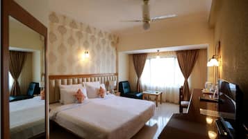 A hotel room with a large bed, a desk with a chair, a television, and a ceiling fan.
