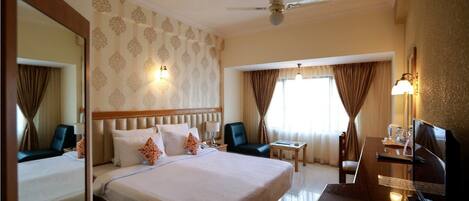 A hotel room with a large bed, a desk with a chair, a television, and a ceiling fan.