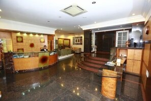 A hotel lobby with a reception desk, a staircase, and a large window.