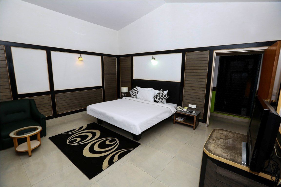 A modern hotel room with a large bed, a TV, a desk, and a green armchair.