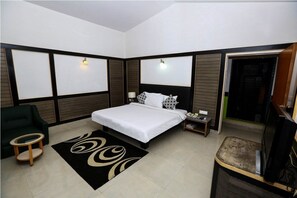 A modern hotel room with a large bed, a TV, a desk, and a green armchair.
