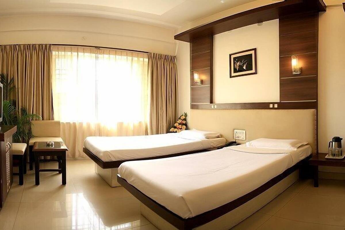 A hotel room with two single beds, a desk with a chair, a television, and a window with curtains.