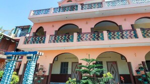A two-story building with a pink facade, multiple balconies with decorative railings, and a covered entrance area with potted plants. - Golden Residency (Bengaluru)