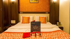 A hotel room with a bed, two pillows, a nightstand, a phone, a framed picture on the wall, and a sign with text. - Golden Residency (Bengaluru)