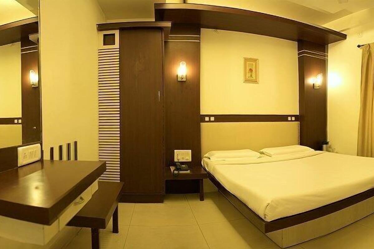 A hotel room with a bed, a desk, a chair, a television, and a mirror.