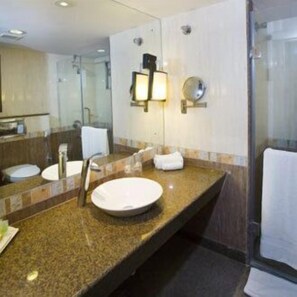 Un baño moderno con encimera de granito, dos lavamanos, un espejo grande y cabina de ducha de vidrio.