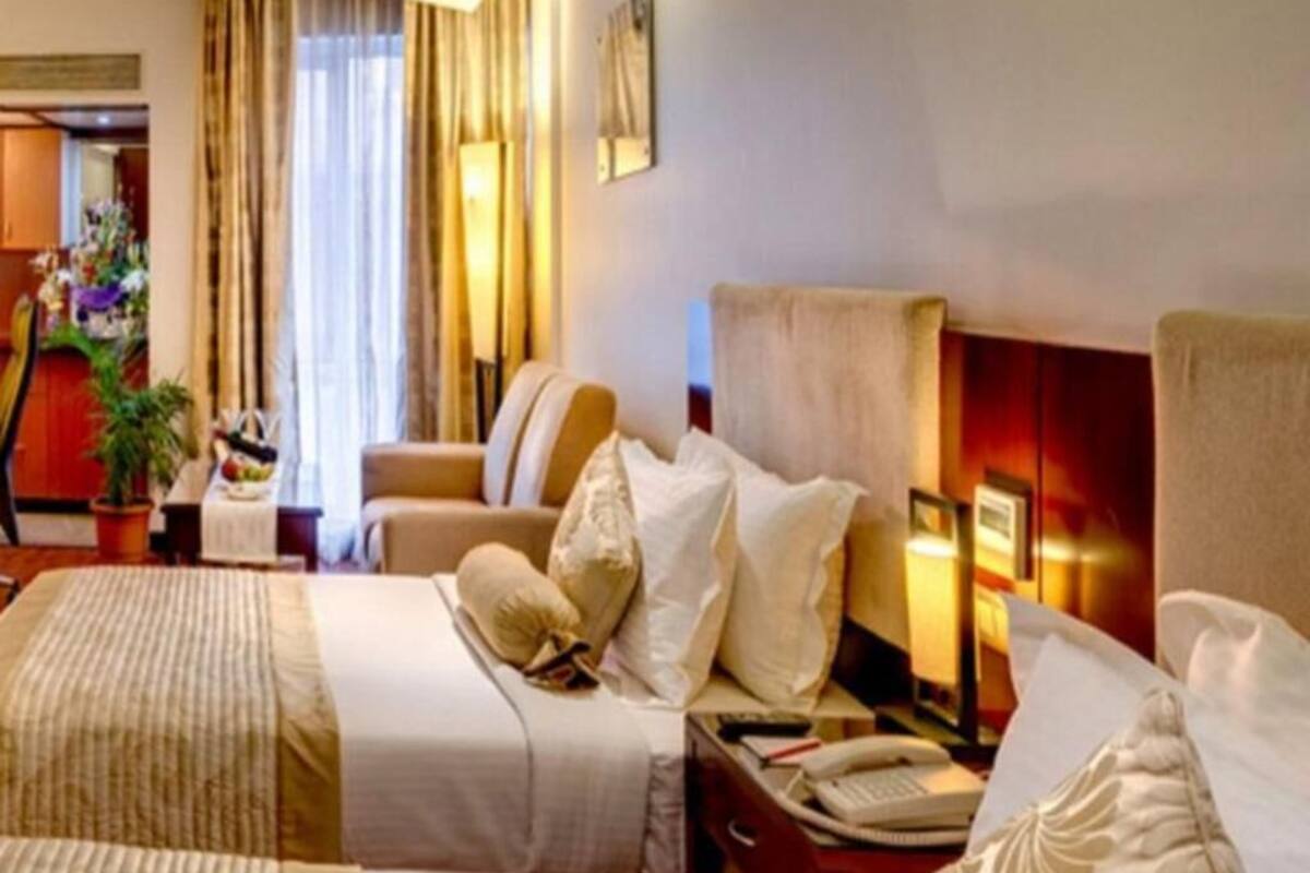 Ein Hotelzimmer mit zwei Betten, einem Nachttisch mit Lampe, einem Sessel und Blick auf den Flur.