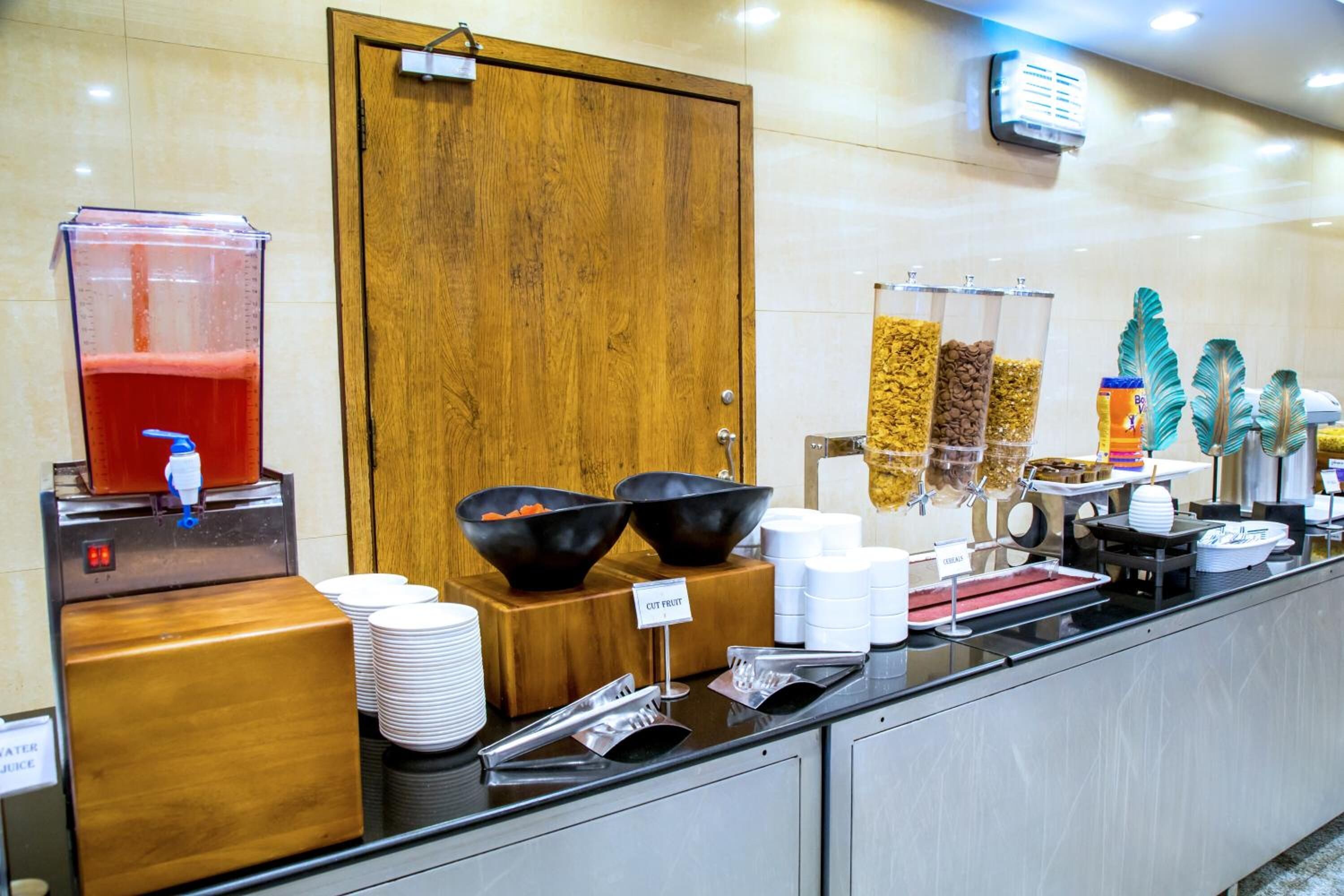 Een buffetopstelling met een waterdispenser, schalen met gesneden fruit en diverse bakken met eten.