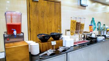Een buffetopstelling met een waterdispenser, schalen met gesneden fruit en diverse bakken met eten.