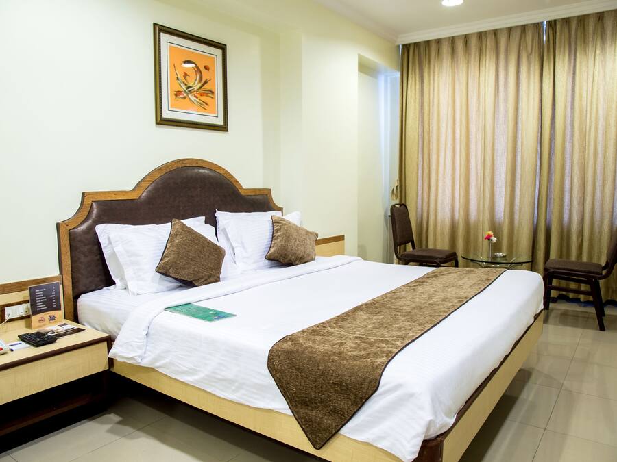 A hotel room with a large bed, a bedside table with a phone and a notepad, a small table with a flower, and a chair.