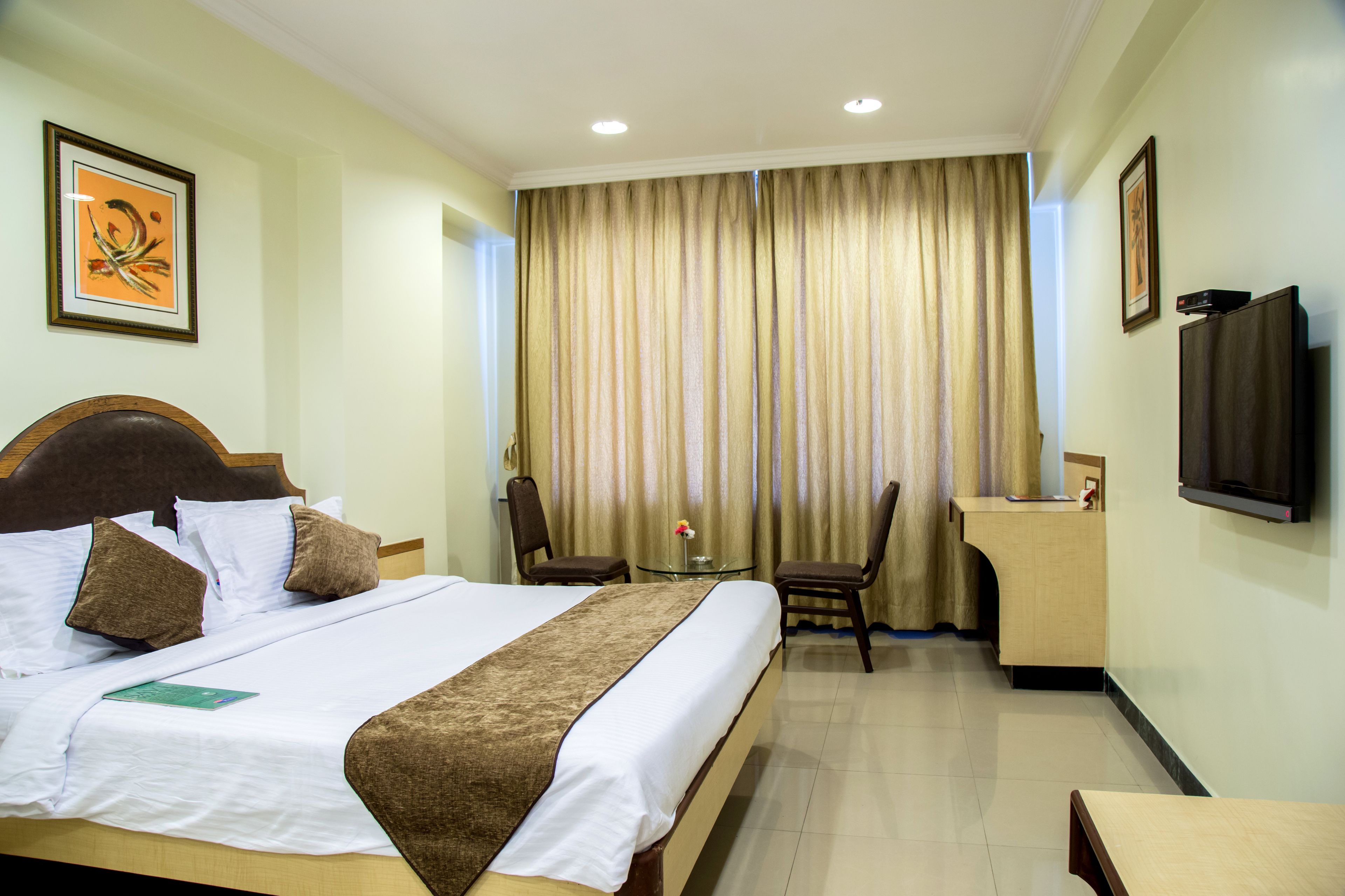 A hotel room with a large bed, a desk, two chairs, a television, and curtains.