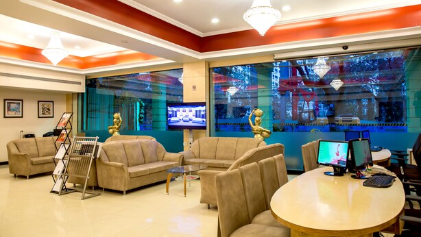 Eine Lobby mit beigefarbenen Sofas, einem runden Tisch mit Computern und einem großen Fenster mit Blick auf ein Gebäude.