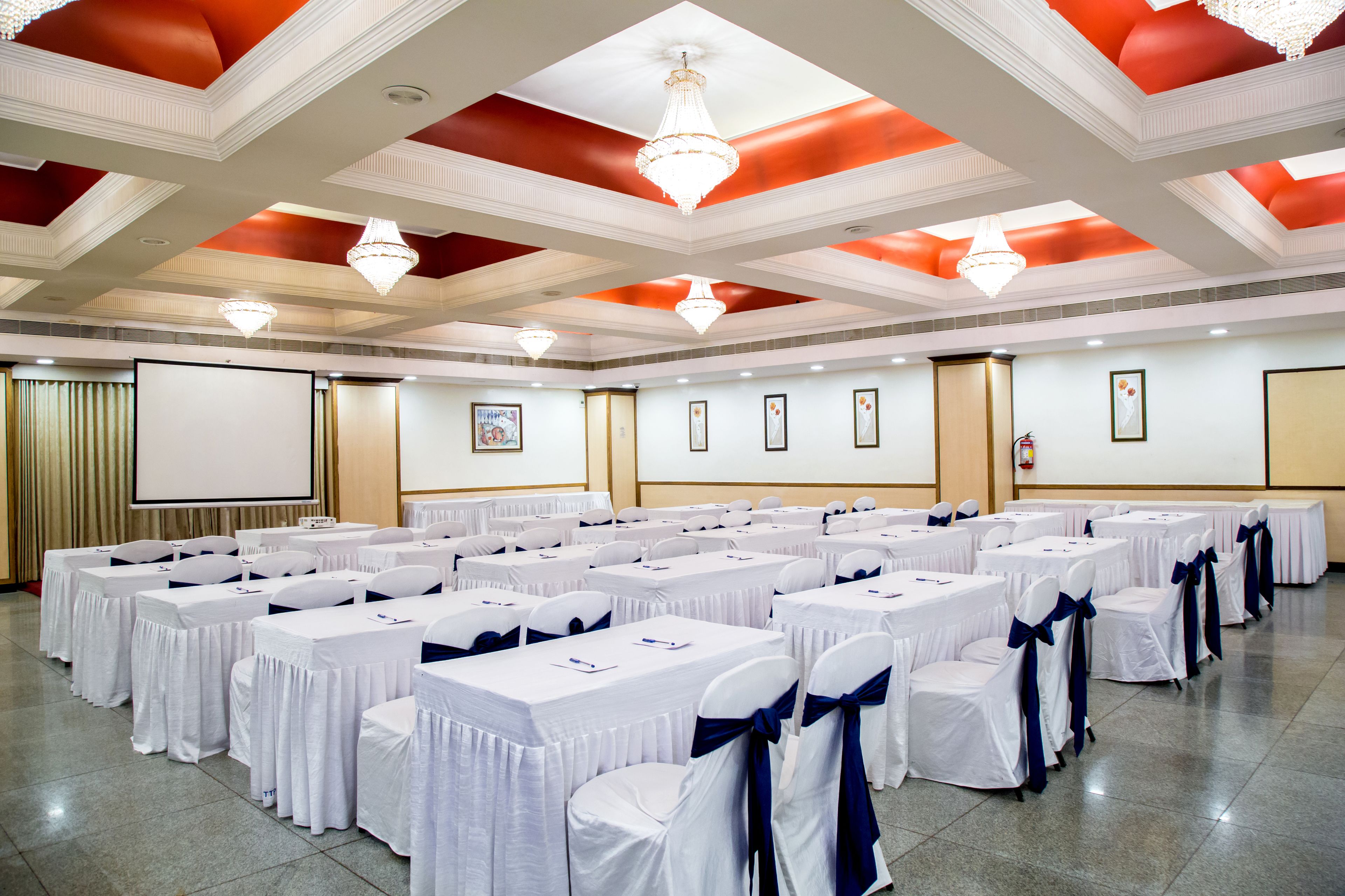 A conference room with rows of tables, white tablecloths, and chairs with blue sashes.