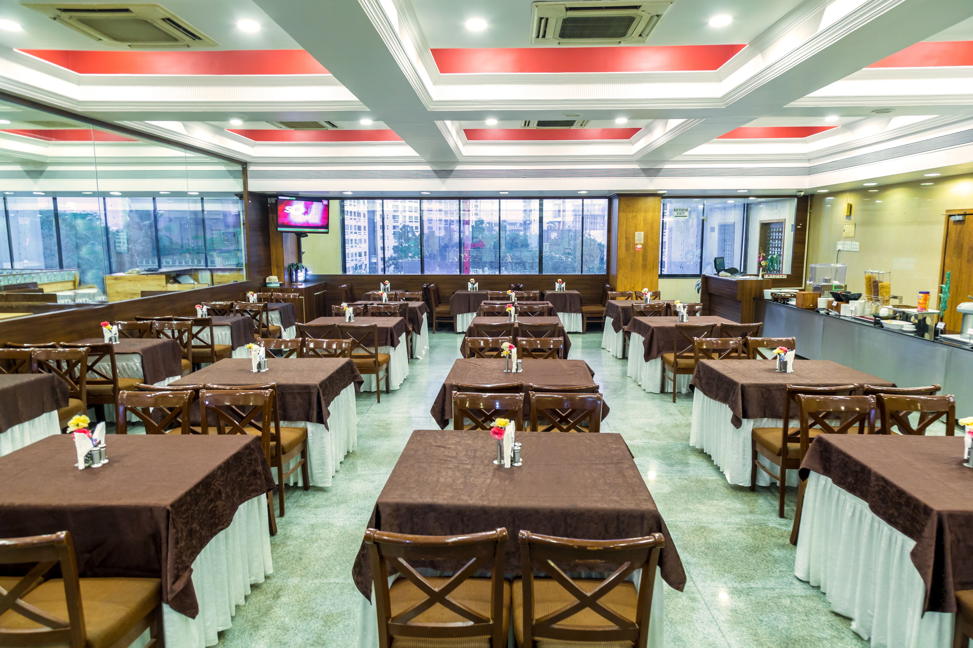Un restaurante con varias mesas y sillas, amplias ventanas con vistas, y una pantalla de televisión.
