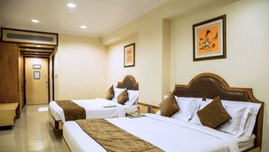 Ein Hotelzimmer mit zwei Betten, jeweils mit einem hölzernen Kopfteil, weißer Bettwäsche und braunen Zierkissen. Es gibt eine Holzbank und einen kleinen Tisch mit einer Blumenvase.