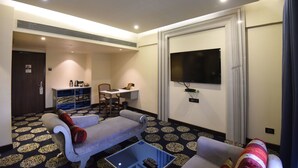 A hotel room with a sofa, a small table, a TV mounted on the wall, and a patterned carpet. - VITS Sharanam, Thane (Thane)