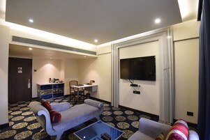 Habitación de hotel con sofá, una mesita, televisor montado en la pared y alfombra estampada.