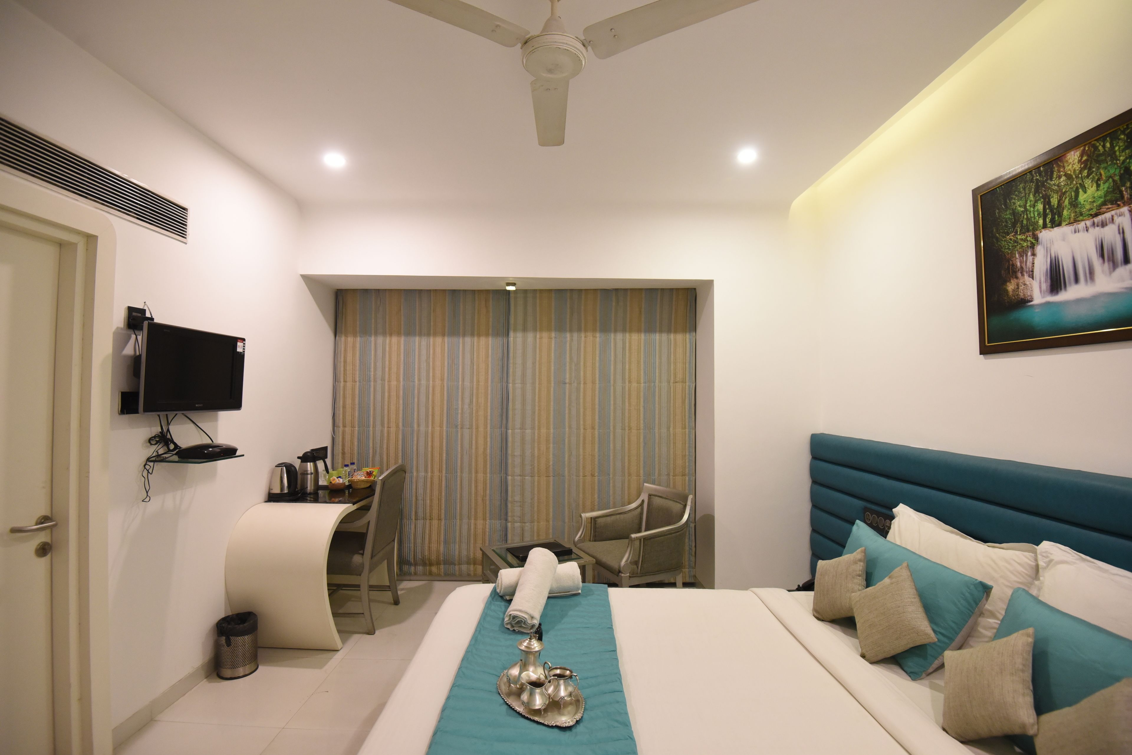 A hotel room with a bed, a desk, a chair, a television, and a painting on the wall.