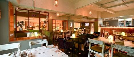 A restaurant with multiple tables and chairs, a bar area, and a television screen.