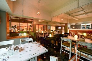 Un restaurante con varias mesas y sillas, una zona de bar y una pantalla de televisión.