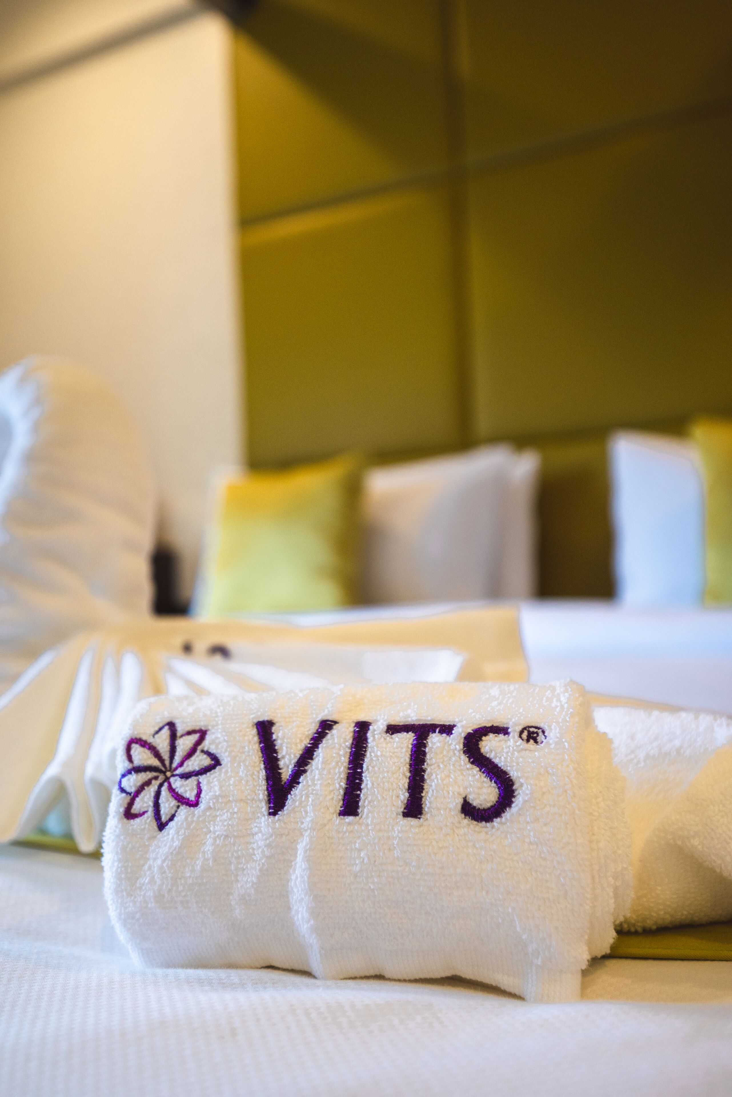 A neatly made bed with a towel that has the word "VITS" embroidered on it.