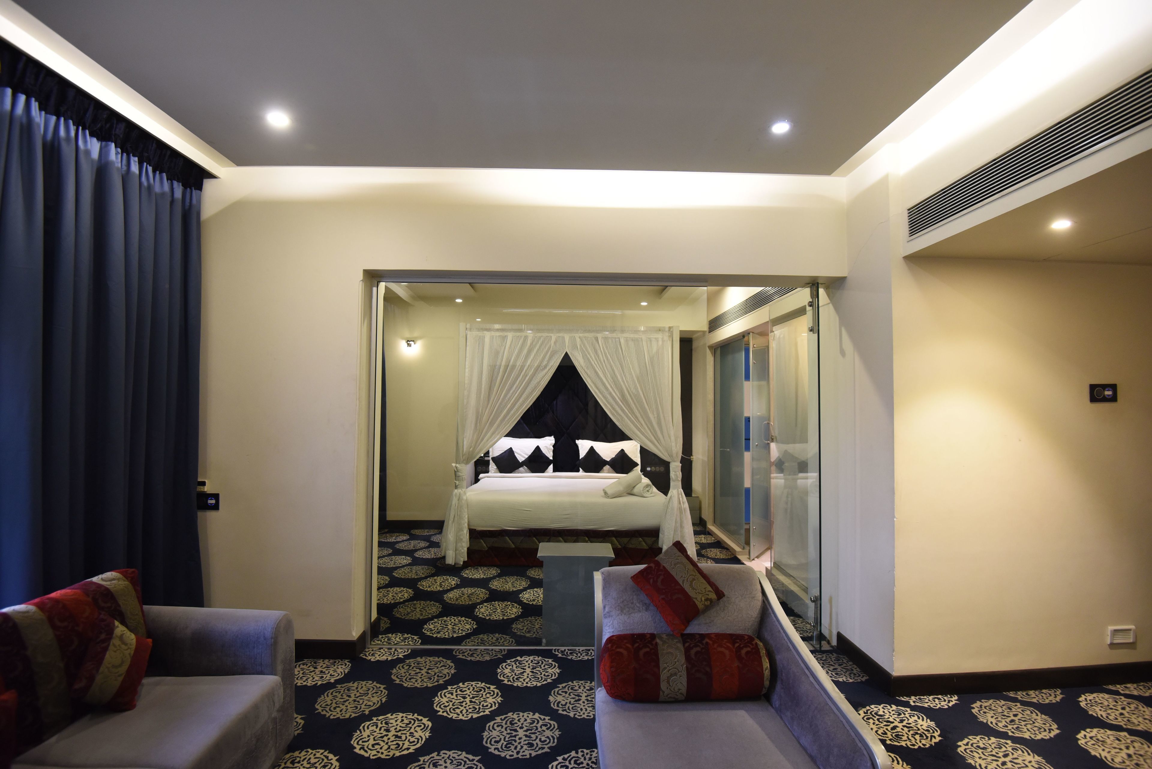 A hotel room with a bed, a sofa, a small table, and a mirror.