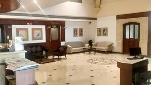 A lobby with a reception desk, sofas, a coffee table, and a patterned floor. - VITS Sharanam, Thane (Thane)