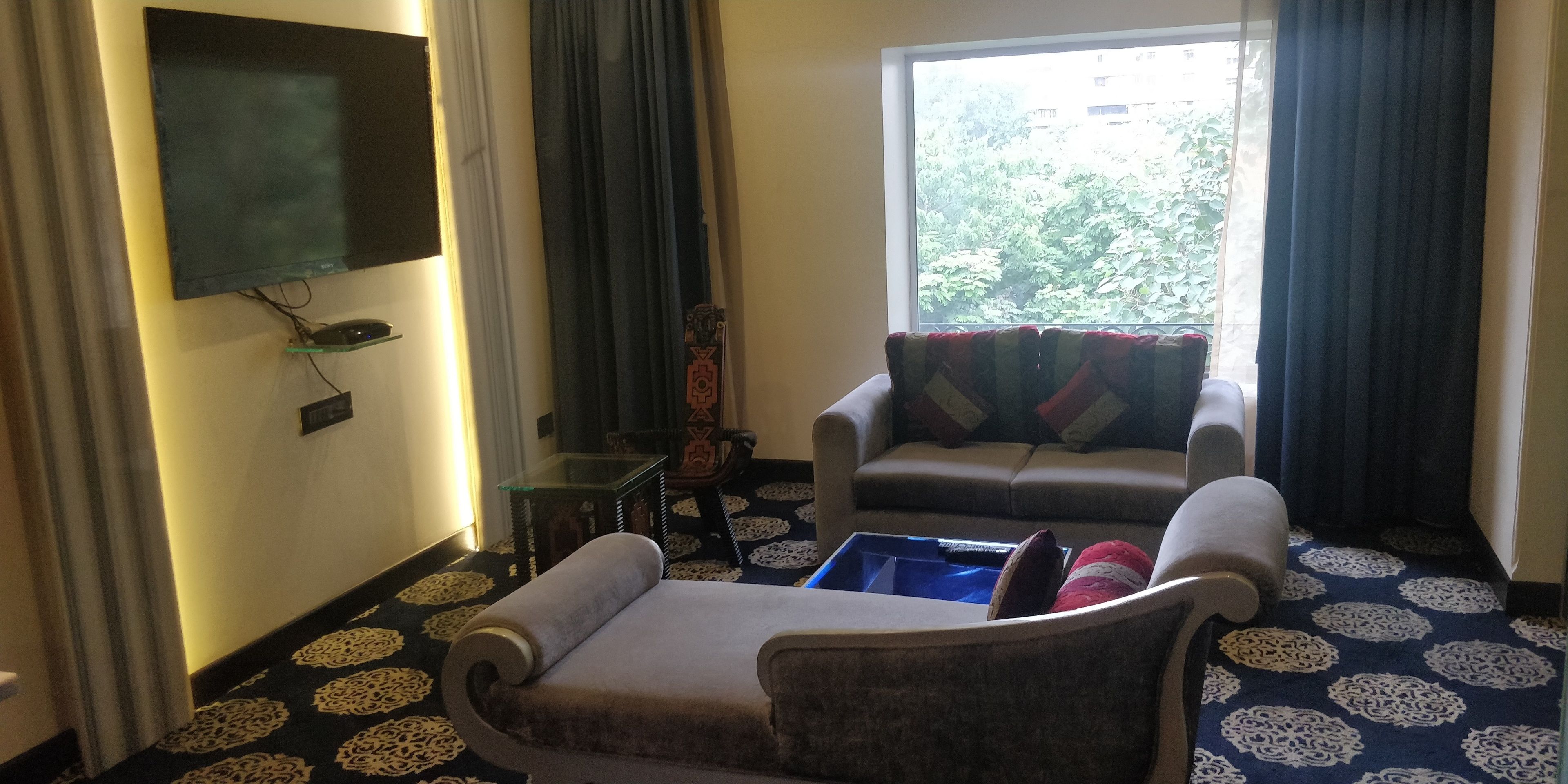 A living room with a sofa, a small table, and a flat-screen TV mounted on the wall.