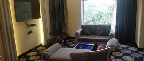 A living room with a sofa, a small table, and a flat-screen TV mounted on the wall.