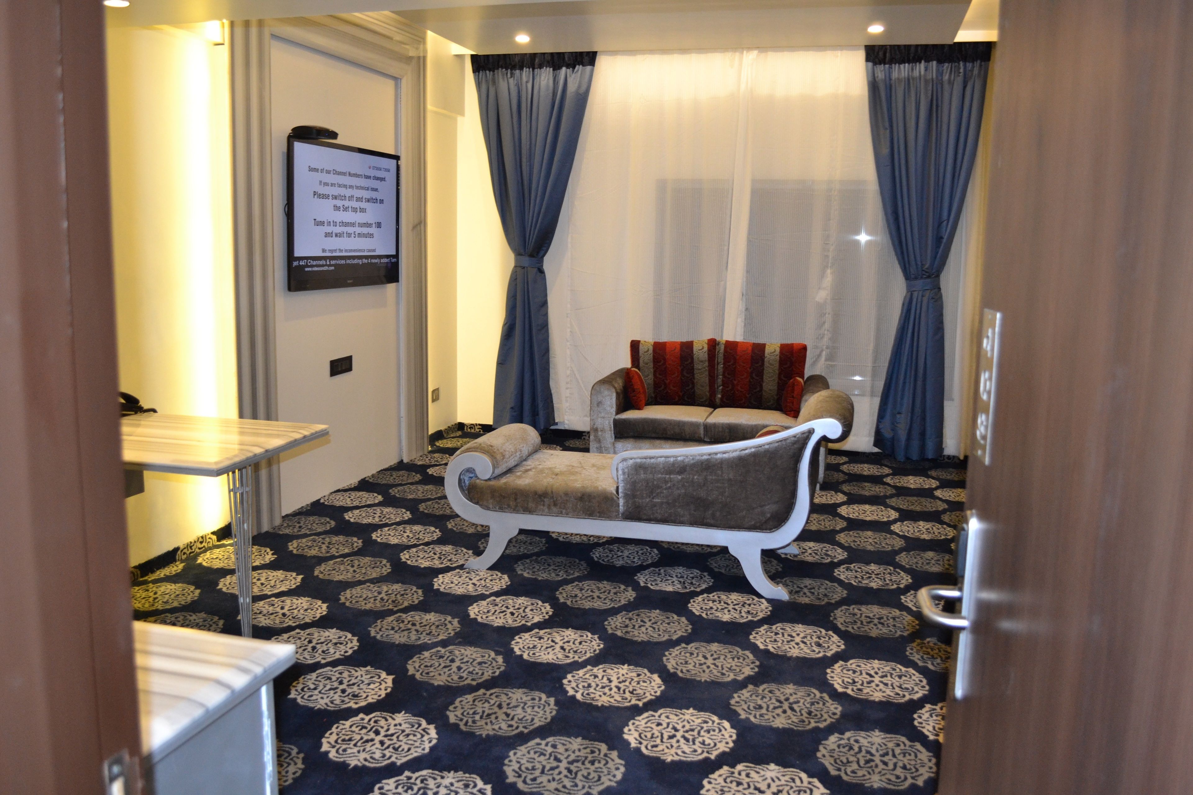 A room with a patterned carpet, a sofa, a small table, and curtains.