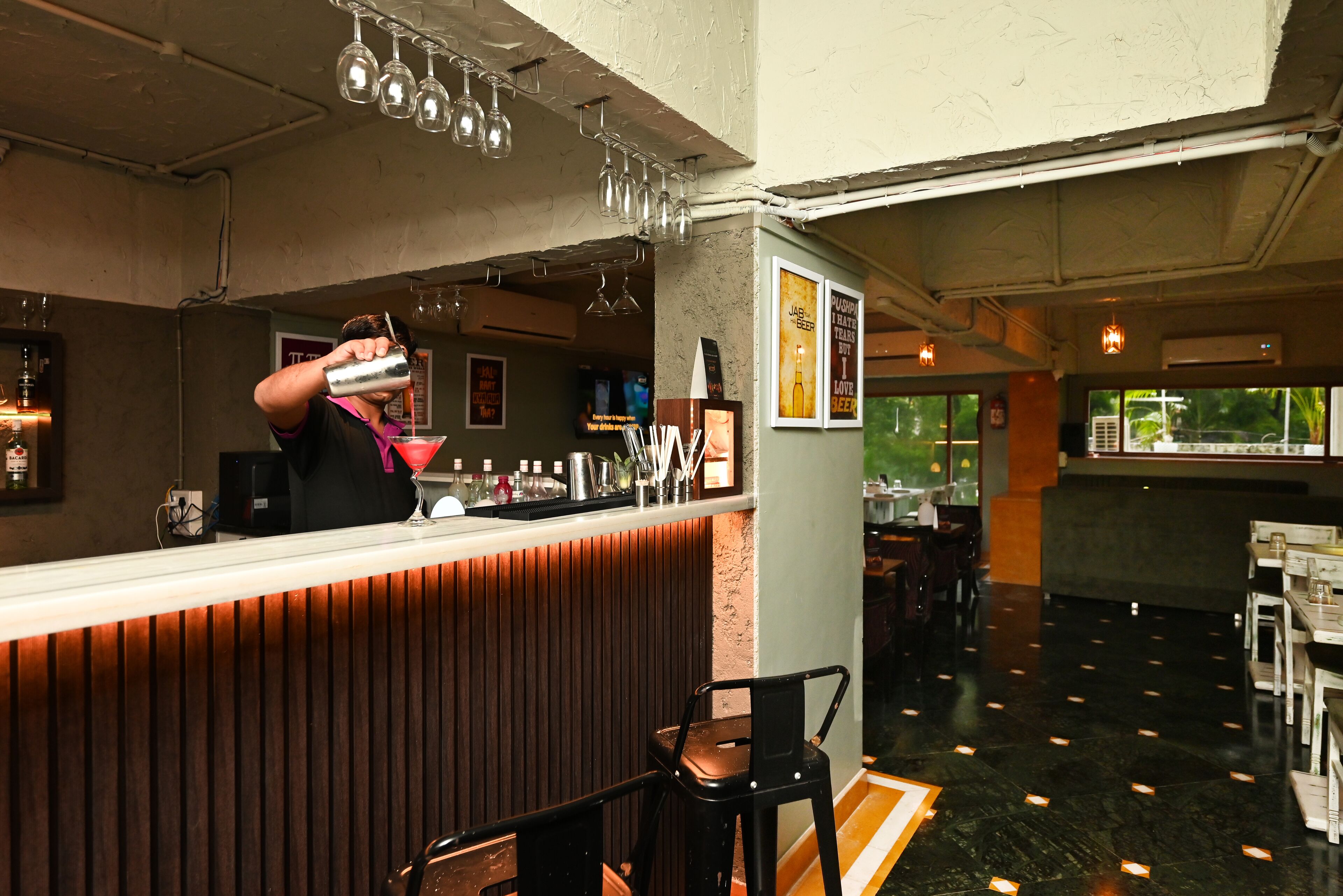 A bar area with a bartender preparing a drink, a wooden counter, and a seating area with tables and chairs.