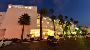 Un hôtel appelé Astral Maris, doté d’un design moderne, de palmiers et d’un espace de stationnement.