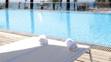 Una piscina al aire libre, sombrillas, sillones reclinables de piscina