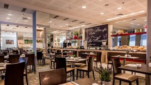 Un café moderne avec des tables et des chaises en bois, un comptoir où l’on sert du café et un tableau affichant le menu.