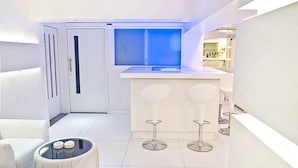 Une cuisine moderne avec une fenêtre illuminée de lumière bleue, des meubles blancs et deux tabourets de bar.