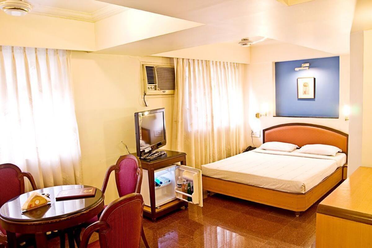 Een hotelkamer met een bed, een televisie, een klein tafeltje met stoelen en een minibar.
