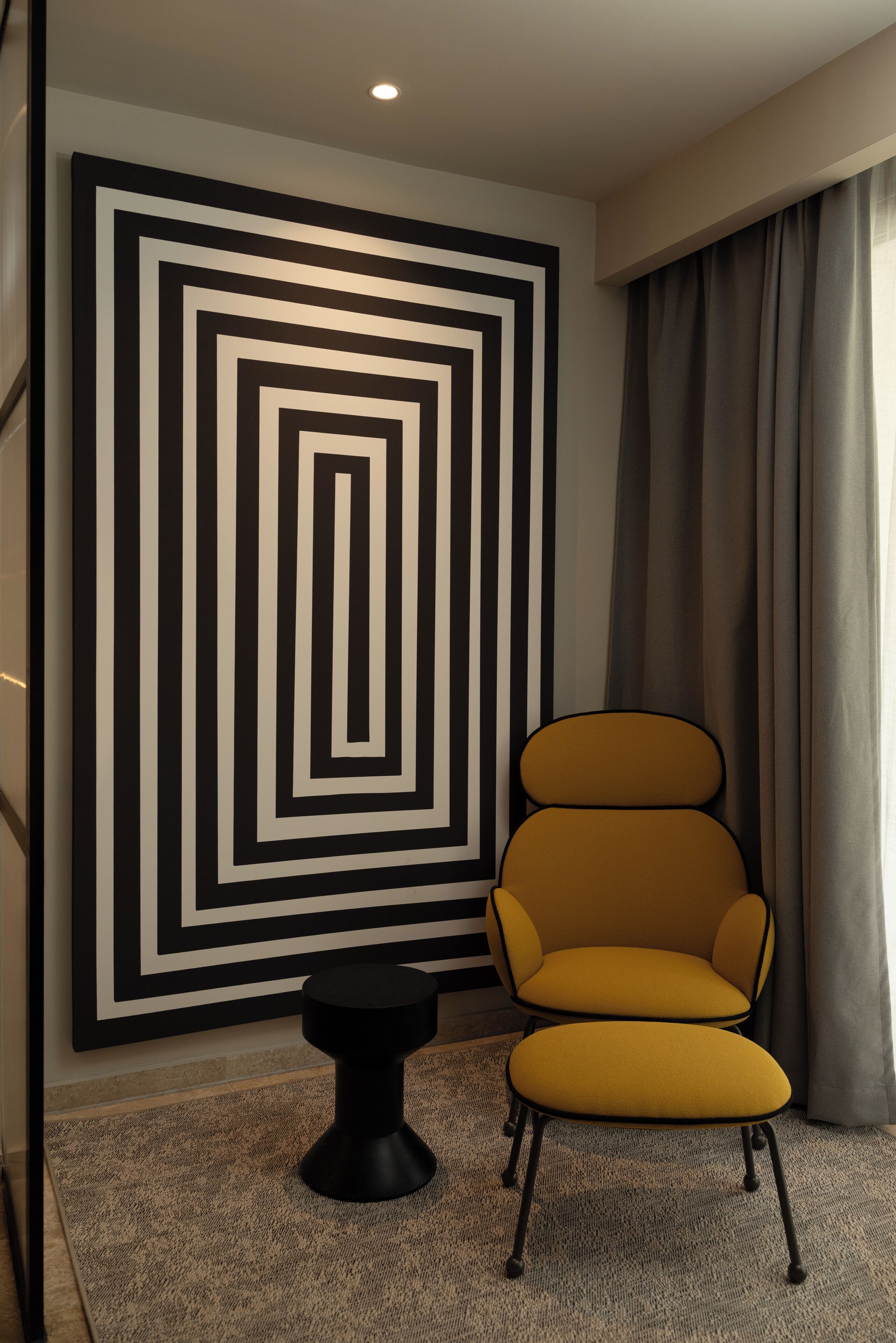 A modern room with a geometric wall art, a yellow armchair, and a small black side table.