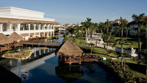 Un resort con un canal de agua, estructuras de techo de paja y un jardín bien cuidado.