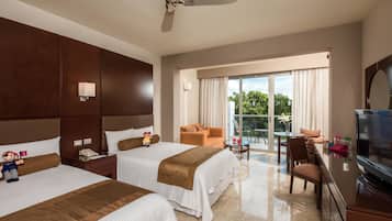 Two double beds with white linens and brown headboards, a flat-screen TV, and a balcony with a table and chairs.